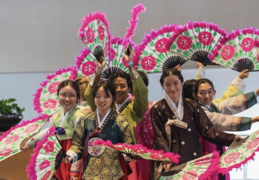 People dress in Korean traditional dress, the hanbok, performing traditional Korean fan dance with large, floral fans.